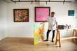© Mint Images - Japanese man standing in art gallery, holding abstract artwork, looking at laptop computer.