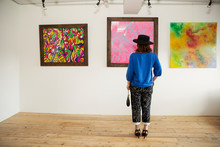 Japanese Woman Wearing Hat Standing In Front Of Abstract Painting In An Art Gallery.