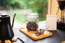 Close Up Of Coffee Pot, Glass Jar With Coffee Beans And Metal Coffee Shovel On Wooden Board.