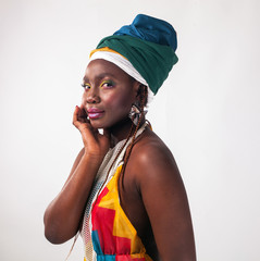 Studio fashion portrait of young African woman in summer dress and ethnic head wrap, white background.