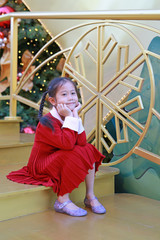 Wall Mural - Pretty Asian little girl in red dress poses in winter season and happy new year festival against christmas background.