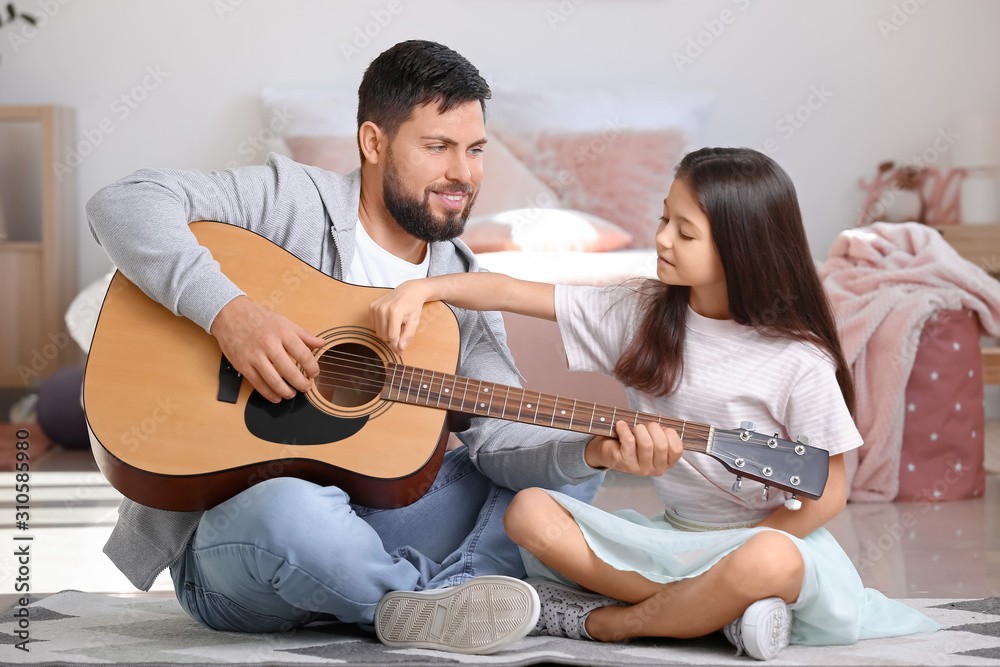 Little daughter and her father playing guitar at home