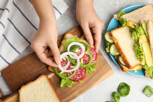 Woman Adding Onion To Tasty Sandwich At Light Grey Marble Table, Top View
