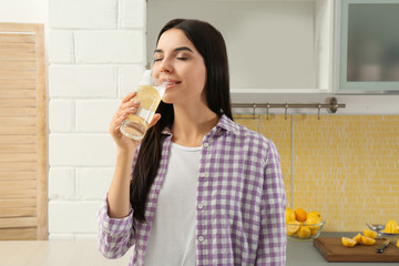 Poster - Beautiful young woman drinking lemon water in kitchen