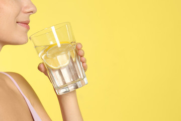 Canvas Print - Young woman drinking lemon water on yellow background, closeup. Space for text