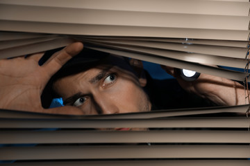 Wall Mural - Male security guard with flashlight looking through window blinds in darkness