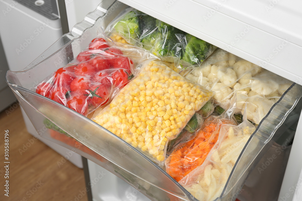 Plastic bags with different frozen vegetables in refrigerator