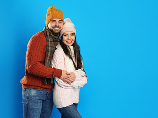 Canvas Print - Happy young couple in warm clothes on blue background, space for text. Winter vacation