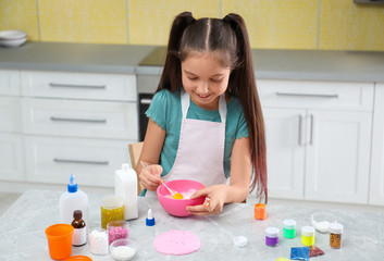 Cute little girl mixing ingredients with silicone spatula at table in kitchen. DIY slime toy