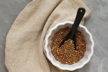 Wall Mural - Buckwheat in A white dish on a wooden gray table. The view from the top. Space for text. delicious and healthy food and nutrition. vitamins for humans. cereals and grains.