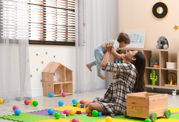 Wall Mural - Young nanny playing with cute little baby at home