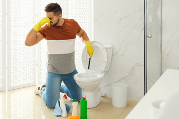 Canvas Print - Young man feeling disgust while cleaning toilet bowl in bathroom