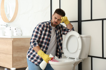 Wall Mural - Young man feeling disgust while cleaning toilet bowl in bathroom