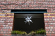 Brick wall with window. White peaky 3D star figure in window of old brick wall overgrown with bare ivy branches. Star shaped lampshade decor. Christmas balcony decoration with green grass. 