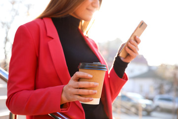 Canvas Print - Businesswoman with cup of coffee and smartphone on city street in morning, closeup