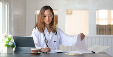 Wall Mural - Cropped shot of female doctor working with tablet and writing on paperwork in office room