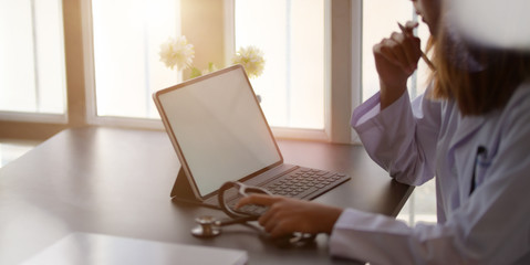 Wall Mural - Cropped shot of female doctor working with tablet and writing on paperwork in office room