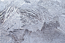 Ice And Frost On A Window Pane In Winter. Pattern From The Leaves Of Fantastic Plants. Crystals Of Frozen Water Close-up. Weather Forecast: Cold, Frost, Cooling. Abstract Light Background Or Wallpaper