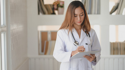 Wall Mural - Young female doctor working on medical records and exam results with tablet