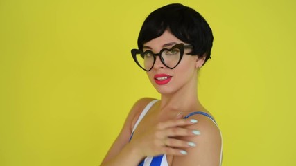 Wall Mural - Brunette in a striped swimsuit posing in the studio on a bright yellow background. Woman in a short wig with sensual lips.