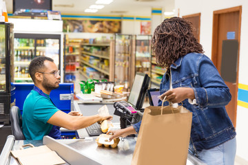 Wall Mural - Serious African American cashier scanning goods at checkout. back view of woman packing products in paper bag. Shopping concept