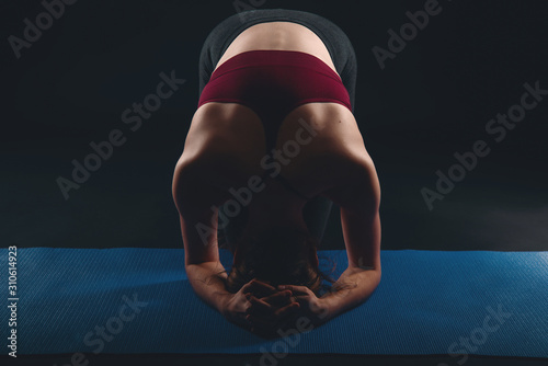 Fotografía Young woman doing yoga in black studio, sirsasana headstand preparation