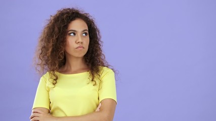 Sticker - Displeased african young woman in yellow t-shirt looking at the camera over purple background isolated 