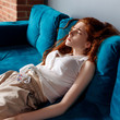 © Dmitrii Kotin - Young redhead woman reclining on the couch and feels tired.