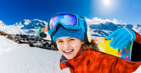 Fototapete - Young girl with ski in winter season, view from ski run at mountains and Val Thorens resort in sunny day in France, Alps.