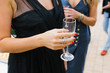 A glass of champagne in the hand of a woman in a black dress at a cocktail reception