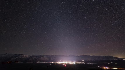 Wall Mural - beautiful time lapse of the stars moving across the night sky. the lights of a small town can be see