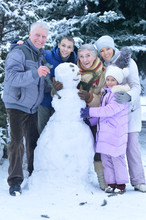 Portrait Of Happy Family In Snow Covered Winter Forest Making Snowman