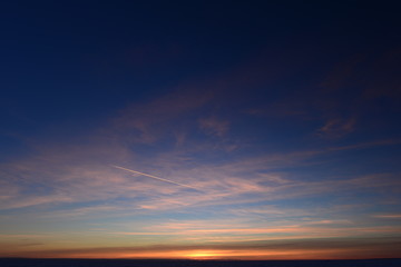 Wall Mural - Airplane trail in the blue sky in white cirrus clouds in winter at sunset