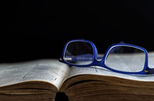 Open Old Book With Reading Glasses On Top, Dark Background.  Reading Concept.