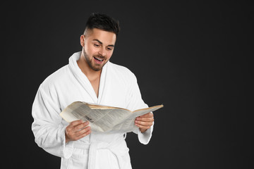 Poster - Young man in bathrobe reading newspaper on black background. Space for text