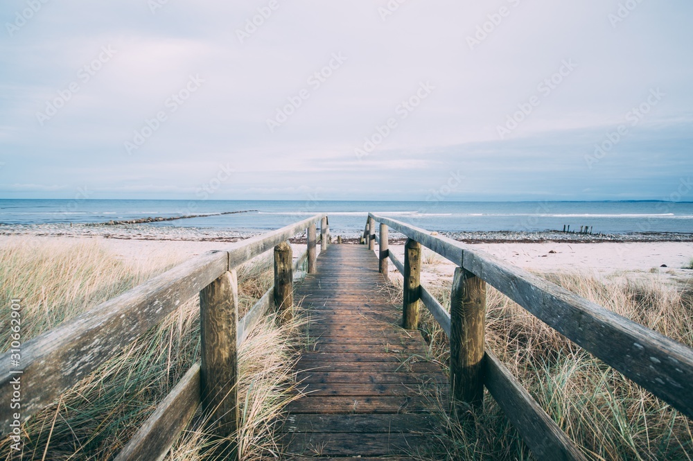 Beautiful scenery of a wooden pathway leading to the beach for a relaxing day - obrazy, fototapety, plakaty 