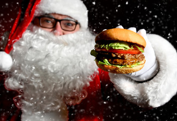 Wall Mural - Happy Santa Claus hold tasty burger sandwich hamburger in hand closeup under snow. New year and Merry Christmas fast food