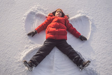 A Child, A Boy, Lies On The Snow, Makes A Snow Angel With His Arms And Legs, Emotions, Laughs