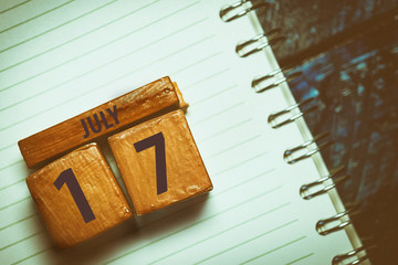 july 17th. Day 17 of month,Handmade wood cube with date month and day placed on a lined notebook on a blue background. artistic coloring.  summer month, day of the year concept