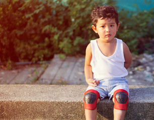 Wall Mural - Asian kid 2 year old from Thailand sitting on the garden alone. He using a safety cycling protection equipment concept. and he looking the wood on his hands.                              