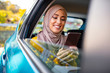 © Dragana Gordic - Muslim business woman in car. Writing a message on her mobile phone. Positive pensive Islamic woman in hijab sitting on backseat of taxi and drinking coffee while using gadget