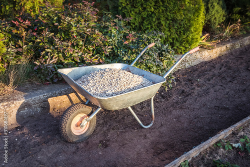 Fotomural Single wheel garden wheelbarrow loaded with crushed stone prepared for garden pa
