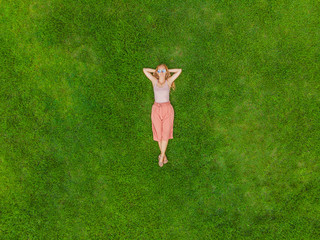 Young woman lying down in the middle of a field and relaxing, drone photo