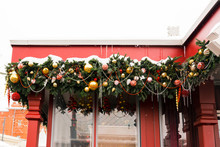 Rectangular Green Decoration Of Christmas Tree Branches, Balls, Garlands And Icicles On Red Wooden Small House