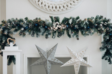 Wall Mural - View over decorated artificial fireplace with decorations inside. Handmade paper stars, candles inside. Beautiful coniferous wreath on the top of fireplace. Decorative round mirror over the fireplace.