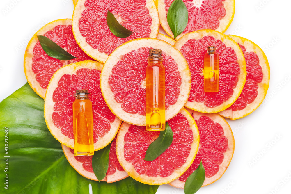Bottles of essential oil and grapefruit slices on white background