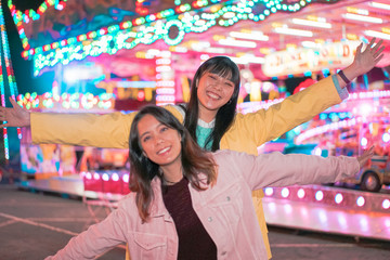 Women as friends visit fair at night and have fun together. Younger girls playing in the luna park. image of two girls in front of abstract blurred background. Image