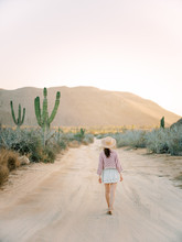 Woman Walking Down Desert Dirt Road At Sunset