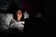 © guille Faingold/Stocksy - Woman lying in bed with laptop in darkness