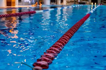 red Swimming Lane Marker in swimming pool.Color-fast swimming pool lane line.Lane ropes in swimming pool.red plastic rope lane on blue water indoor pool sport competition background. selective focus